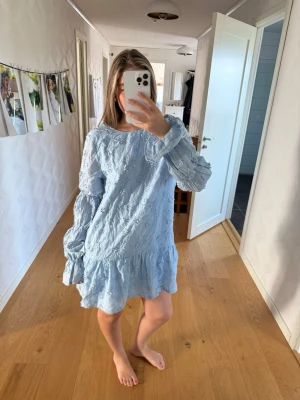 Ljusblå volangklänning med spets - Supersöt ljusblå kortklänning med volangkant och långa puffärmar. Klänningen har fina spetsdetaljer över hela tyget och en lös passform som ger en avslappnad men ändå trendig look. Perfekt för sommarens alla tillfällen!