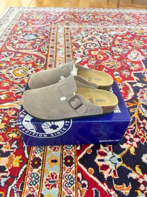 Birkenstock Boston grey - Säljer ett par snygga beigea Birkenstock tofflor i storlek 38. De har en klassisk slip-in modell med justerbart spänne i metall och bekväm korksula. Skickar samma dag eller nästa 