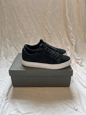 Svarta sneakers i mocka från Vagabond - Stilrena svarta sneakers i mocka från Vagabond med vit sula och klassisk låg profil. Skorna har svarta skosnören och en enkel, tidlös design som passar till många olika outfits. Perfekta för dig som gillar en clean och modern look.