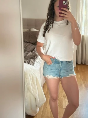 Blåa Levi's jeansshorts - Säljer ett par klassiska blå jeansshorts från Levi's med hög midja och slitna, fransiga kanter. De är i mycket bra skick!