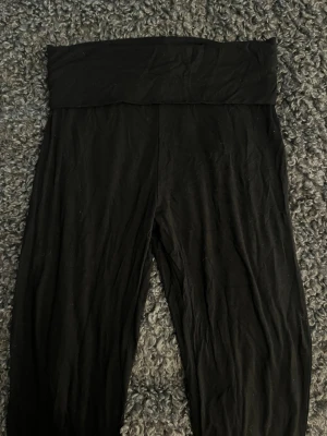 Svarta yoga byxor med låg midja - Säljer ett par svarta yoga byxor med bred, hög midja och stretchigt material. Perfekta för en avslappnad och bekväm stil. Passar till det mesta och är superenkla att matcha med olika outfits.