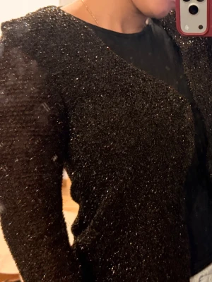 Glittrig brun stickad tröja - Säljer en brun stickad tröja med glittriga inslag. Tröjan har lång ärm och är gjord i ett mjukt, stretchigt material som ger en snygg och bekväm passform. Perfekt för dig som vill ha något extra till din outfit.