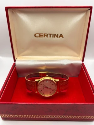 Certina guldfärgad klocka - Stilren Certina klocka med guldfärgat metallarmband och rund silverfärgad urtavla. Klockan har datumvisning och klassisk design med minimalistiska index. Perfekt accessoar för dig som gillar tidlös och elegant stil.