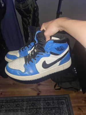 Nike air jordan high  - Säljer ett par höga sneakers i blått och vitt med svarta detaljer och snörning. Skorna har en klassisk siluett med svart swoosh på sidan och perforerad tåbox. Yttermaterialet är en mix av läder och syntet. Perfekta för dig som gillar streetwear och sportig stil.