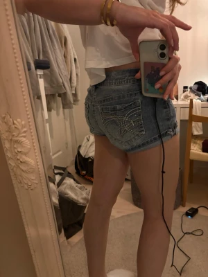 Lågmidjade blå jeansshorts med detaljer - Säljer ett par riktigt snygga lågmidjade jeansshorts i ljusblå denim. Shortsen har dekorativa sömmar och glittriga detaljer på bakfickorna💝