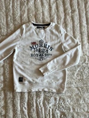 Morris sweatshirt med tryck i offwhite - stl M - Morris sweatshirt med tryck i offwhite, storlek M. 75% bomull, 25% polyester, ruggad insida. Stort tryck fram och tygflagga på bröstet. Personen på bilden är 189cm, väger 78kg.  Använd men i mycket fint skick, inga hål eller fläckar.  Rök- och djurfritt hem. Skriv gärna om du vill ha fler bilder eller undrar något!