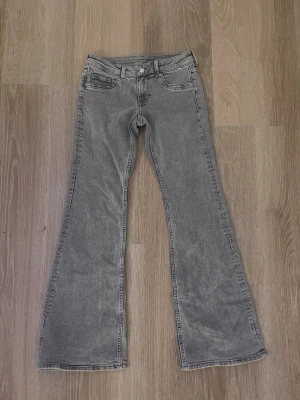 Grå bootcut jeans med låg midja - Säljer ett par knappt använda grå bootcut jeans med låg midja. Jeansen har utsvängda ben och är tillverkade i ett mjukt denimtyg som ger en avslappnad vibe. Perfekta för dig som gillar retrostilen och vill ha ett par snygga jeans i garderoben. 