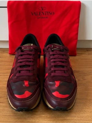 Valentino Rockrunners  - Box och dustbag medföljer, pris går att diskutera vid snabb affär.Snygga sneakers från Valentino Garavani i vinrött och rött med kamouflagemönster. Skorna har låga skaft, svarta detaljer och beige sula. Materialmix av mocka och textil ger en exklusiv känsla. 
