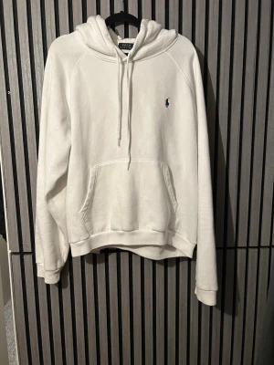 Vit hoodie från Polo Ralph Lauren - Säljer en stilren vit hoodie från Polo Ralph Lauren med klassisk huva och dragsnören. Tröjan har en känguruficka framtill och den ikoniska lilla broderade loggan på bröstet. Den är stor på brädden (XXL) men på längden är de perfekt om du är 180 pris kan diskuteras!