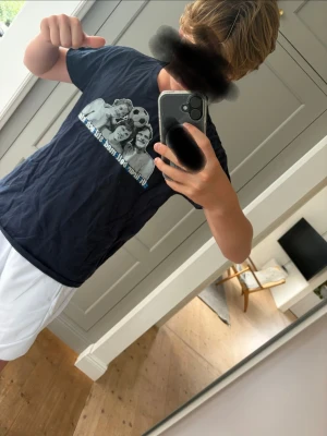 Mörkblå t-shirt med tryck - Säljer en mörkblå t-shirt med ett stort tryck framtill som visar Djurgården tifo mot Hammarby 2024. T-shirten har korta ärmar och en klassisk passform. Perfekt för dig som gillar sportiga och avslappnade plagg.