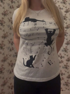 Vit t-shirt med svarta katter och noter - Säljer en vit t-shirt med korta ärmar och tryck av svarta katter som leker bland noter och notrader❣️ T-shirten har en klassisk passform och är gjord i mjuk bomull, jag säljer den eftersom jag inte använt den så mycket❣️Jag vet tyvärr inte vart den kommer ifrån, eftersom jag fick den från en släkting för något år sedan💕