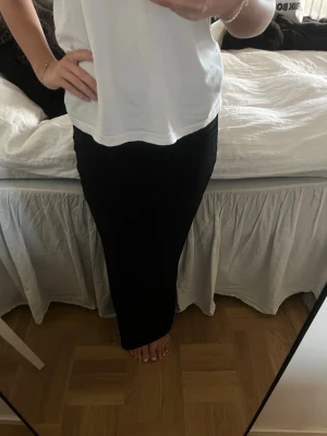 Svart långkjol i enkel design - Säljer en svart långkjol med rak passform. Kjolen har en stilren och minimalistisk look som passar till många olika outfits. Materialet känns mjukt och följsamt, perfekt för dig som gillar en clean och klassisk stil.
