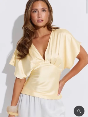 Ljusgul omlottopp i satin - Snygg ljusgul omlottopp i satin med djup v-ringning och korta, vida ärmar. Från gina tricot. Endast testad så i nyskick