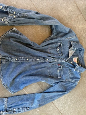 Klassisk jeansskjorta i blå denim - En super skön blå jeansskjorta i denim från Levi’s med två bröstfickor och vita knappar. Skjortan har lång ärm och en avslappnad passform. Perfekt till ett par svarta jeans eller shorts, cowboy tema eller för en cool vardagslook. Knappt använd och säljer pågrund av garderobs-utrensning😊 