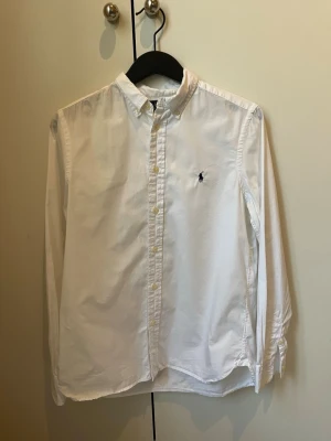 Vit Ralph Lauren skjorta i storlek 158-164cm 13-14 år - Säljer en vit skjorta från Ralph Lauren i storlek 158-164 13-14cm år. Säljer denna skjorta för att den är för liten, skjortan är använd få tal gånger och är i mycket bra skick 