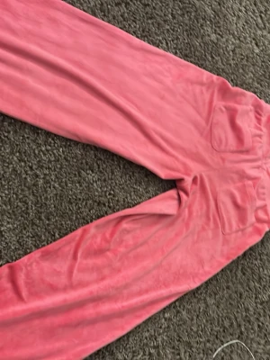 Rosa mjukisbyxor med dragsko - Säljer ett par rosa mjukisbyxor i mjukt velourmaterial. Byxorna har raka ben, bred resår i midjan med dragsko och två stora fickor framtill. Perfekta för chill dagar hemma eller när du vill vara extra bekväm.