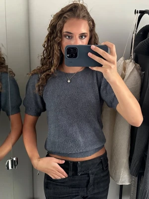 Grå stickad topp med puffärm - Säljer en grå stickad topp med korta puffärmar och rund hals. Tröjan har en croppad passform och är gjord i mjukt stickat material. Perfekt till jeans eller kjol för en trendig look.