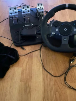 Logitech G290 pc/Xbox - Säljer en Logitech ratt och pedalset för Xbox. Ratten är svart med detaljer i metall och har flera knappar, inklusive Xbox-knappar. Pedalerna är i metall och svart plast, med tre pedaler för realistisk racingkänsla. Perfekt för racing- och bilspel. Du får en extra snabb sladd plus skydd till ratten så du undviker damm ( damm=stickdrift).