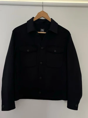 Svart overshirt från Zara - Stilren svart overshirt från Zara med klassisk krage och två bröstfickor med lock och knapp. Rak passform och knäppning framtill. Aldrig använd. Storlek M. Hör av dig vid frågor.  