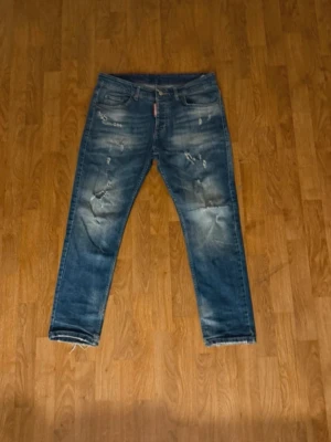 Blå slitna jeans med distressed detaljer - Säljer ett par blå jeans med snygga slitningar och distressed detaljer framtill. Jeansen har klassisk femficksmodell och raka ben. Perfekta för en avslappnad och trendig look. Materialet är denim i bomull.