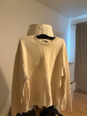 Krämvit stickad tröja från Zara - Säljer en krämvit stickad tröja från Zara med rund halsringning och ribbade muddar. Tröjan har en avslappnad passform och långa ärmar, perfekt för lager på lager under kyligare dagar.