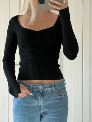Svart ribbad tröja med sweetheart-ringning - En svart ribbad tröja med lång ärm och snygg sweetheart-ringning. Figurnära passform, stretchigt material och en liten slits i ärmen :) lite liten i storleken