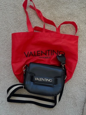 Valentinoväska - Så nice svart axelväska från Valentino med justerbar bred axelrem i svart och vitt. Inte alls använd många gånger så den är i väldigt väldigt bra skick. Tillkommer med den röda dustbagen! 