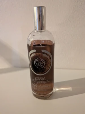 Coconut Body Mist från The Body Shop - Fräsch Coconut Body Mist från The Body Shop med en söt och tropisk doft av kokos. Kommer i en genomskinlig glasflaska med silverfärgad spraykork och brunt etikettmotiv. Se bild för hur mycket som är kvar, flaskan är 100 ml