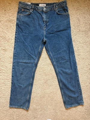 Blå jeans från Just Junkies - Endast använda en gång, så nyskick! Klassiska blå jeans från Just Junkies i rak modell. Jeansen har fem fickor, bälteshällor och stängs med knapp och dragkedja. Tillverkade i slitstarkt denimtyg med snygga kontrastsömmar. Perfekta för en avslappnad och trendig look.