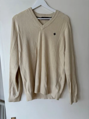 Morris tröja - Klassisk beige V-ringad tröja från morris med diskret logga broderad på bröstet. Tröjan har långa ärmar och ribbade muddar vid ärmslut och nederkant. size m men passar s Perfekt för en stilren och enkel look.