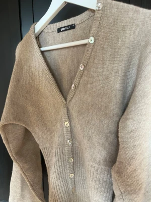 Beige kofta från Gina Tricot oanvänd! - Helt ny tröja ifrån ginatricot! Mysig beige kofta med v-ringning och ribbstickad midja. Koftan har långa ärmar och knappar framtill i olika nyanser. Perfekt för lager på lager och enkel att matcha med jeans eller kjol.