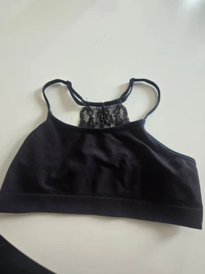 Svart bralette med spetsdetalj - En svart bralette med tunna axelband och dekorativ spets i ryggen. Mjuk och bekväm modell utan byglar, perfekt för dig som gillar en enkel men snygg look. Materialet är stretchigt och följsamt, och spetsen ger en extra fin touch.