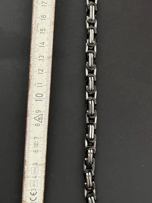 Tungt kedjearmband i metall - Snyggt armband i rostfritt stål med robust kedjedesign. Färgen är en mix av silver och svart, vilket ger en cool och modern look. Länkarna är rejäla och armbandet har ett klassiskt lås. Perfekt för dig som gillar en lite tuffare stil.