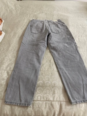 Ljusgrå raka jeans - Säljer ett par ljusgrå jeans med rak passform och klassisk femficksdesign. Jeansen har bälteshällor och stängs med dragkedja och knapp. 