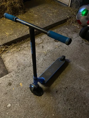 Blå och svart trick sparkcykel - Säljer en blå och svart trick sparkcykel med T-styre och greppvänliga handtag. Den har en robust metallram och små hjul som passar för tricks och skatepark. Perfekt för dig som gillar att åka sparkcykel och testa nya tricks.