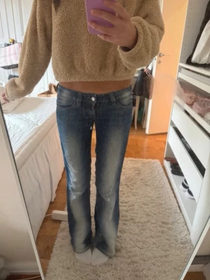 Blå bootcut jeans med slitningar - Säljer ett par blå bootcut jeans med snygga slitningar och ljusa partier framtill. Jeansen har normal passform och klassisk femficksdesign. (Liten slitning i skrevet, men inget man tänker på).
