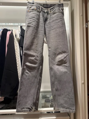 Grå raka jeans med fem fickor - Säljer ett par grå jeans med rak passform och klassisk femficksdesign. Jeansen har bälteshällor, knappgylf och är tillverkade i ett slitstarkt denimtyg. Perfekta för en avslappnad och trendig look.