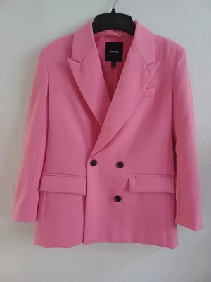 Fuchsia pink blazer - Stylish fuchsia pink tailored blazer with decorative pocket flaps and padded shoulders. Elegant structured fit, perfect for adding a statement touch to any outfit.  Size: XS / 34 Condition: Very good — less than 1 cm pen mark on the right shoulder. The colour inside the collar around the hanging loop is slightly faded and worn, but this is not visible when wearing the blazer. Colour: Fuchsia pink Material: Polyester  Perfect for work, dinners, events or adding a stylish touch to everyday life.
