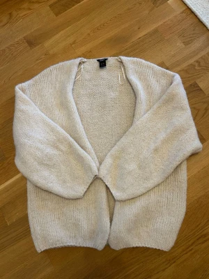  Ny slutsåld Beige stickad öppen kofta från Lindex  - Mysig beige stickad kofta med öppen front och lång ärm. Koftan har en avslappnad passform och är tillverkad i ett mjukt, fluffigt material som känns skönt mot huden. Perfekt att slänga på sig när det är lite kyligt ute.