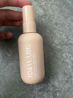 IDA WARG Moisture Hair Serum - Fuktgivande hårserum från IDA WARG i en beige plastflaska med pump. Produkten är vegansk och har en återfuktande formula som passar alla hårtyper. Flaskan rymmer 100 ml och har stilren design med vit text.