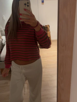 Randig croppad långärmad topp - Säljer en croppad topp med lång ärm i mörkrosa och mörkgröna ränder. Toppen har en avslappnad passform och är perfekt för dig som gillar en trendig och bekväm stil. Passar till både jeans och mjukisbyxor.