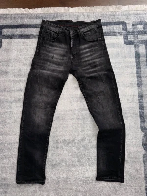 Svarta slim fit jeans med slitningar - Säljer ett par svarta slim fit jeans med snygga slitningar och tvättade detaljer. Jeansen har fem fickor, normal midja och raka ben. Materialet är denim med stretch för extra komfort. Perfekta för en trendig och avslappnad stil.