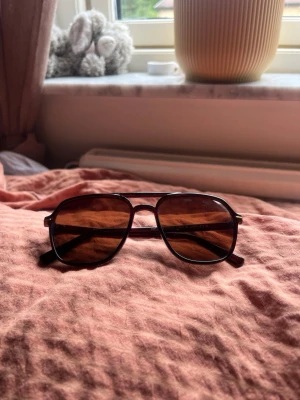 Mörkbruna solglasögon - Snygga solglasögon i aviator-modell fast tjockare bågar med bruna glas och mörkbrunt plastbåge. Glasen är lätt tonade och bågarna har en stilren, tidlös design som passar till de flesta outfits.