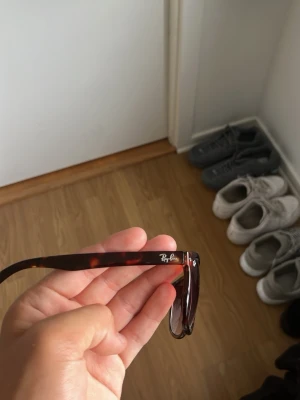 Ray-Ban bruna solglasögon - Snygga solglasögon från Ray-Ban med klassisk wayfarer-form. Bågarna är bruna med sköldpaddsmönster och glasen är mörka. Perfekta för soliga dagar och ger en cool vibe till din outfit.
