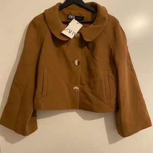 Brun jacka/kavaj från Zara - NWT. Jacka med lätt flare armar och guldiga knappar. Går till höften cirka. Peter pan krage. 