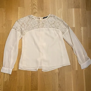 En ljusrosa blus, storlek 36 - En ljusrosa tunn tröja. Mönster som är lite liknande blommor vid axlarna och ovanför brösten. En knapp på handleden på varje arm. En knapp vid nacken/kragen på baksidan av tröjan samt tre rosetter på baksidan. Mellan rosetterna är tröjan öppen. Aldrig använd. Köpt från boohoo o storlek 36