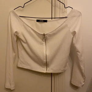 Långärmad vit topp - Långärmad vit topp med stilren dragkedja i mitten, toppen går ej över axlarna. Köpare står för frakten.