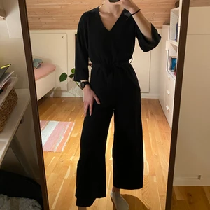 Svart byxress Monki - Svart byxdress från Monki, v-ringad med knytskärp. Storlek xxs, jag är 165 cm lång.