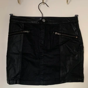 Svart kort kjol, strl 34 - Svart snygg tyg/skinnkjol med dragkjedjor i strl 34.