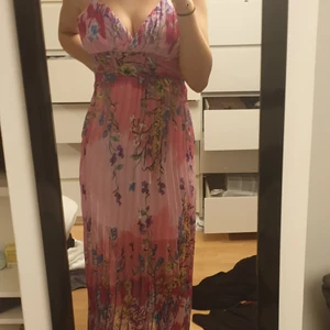 Klänning - Rosa långklänning med mycket färgade blommor på, säljs pågrund av att den ej kommer till andvändning och bara andvänds 1 gång, luftigt matrial, frakt tillkommer på 66kr (spårbar)